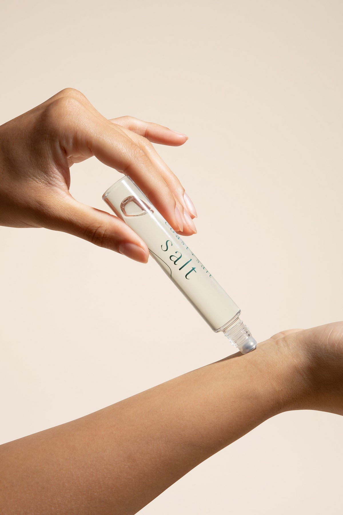 Hand applying Salt perfume roller to wrist on a neutral background