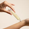 Hand applying a clear bottle labeled 'Sunset Sorbet' above an arm on a beige background