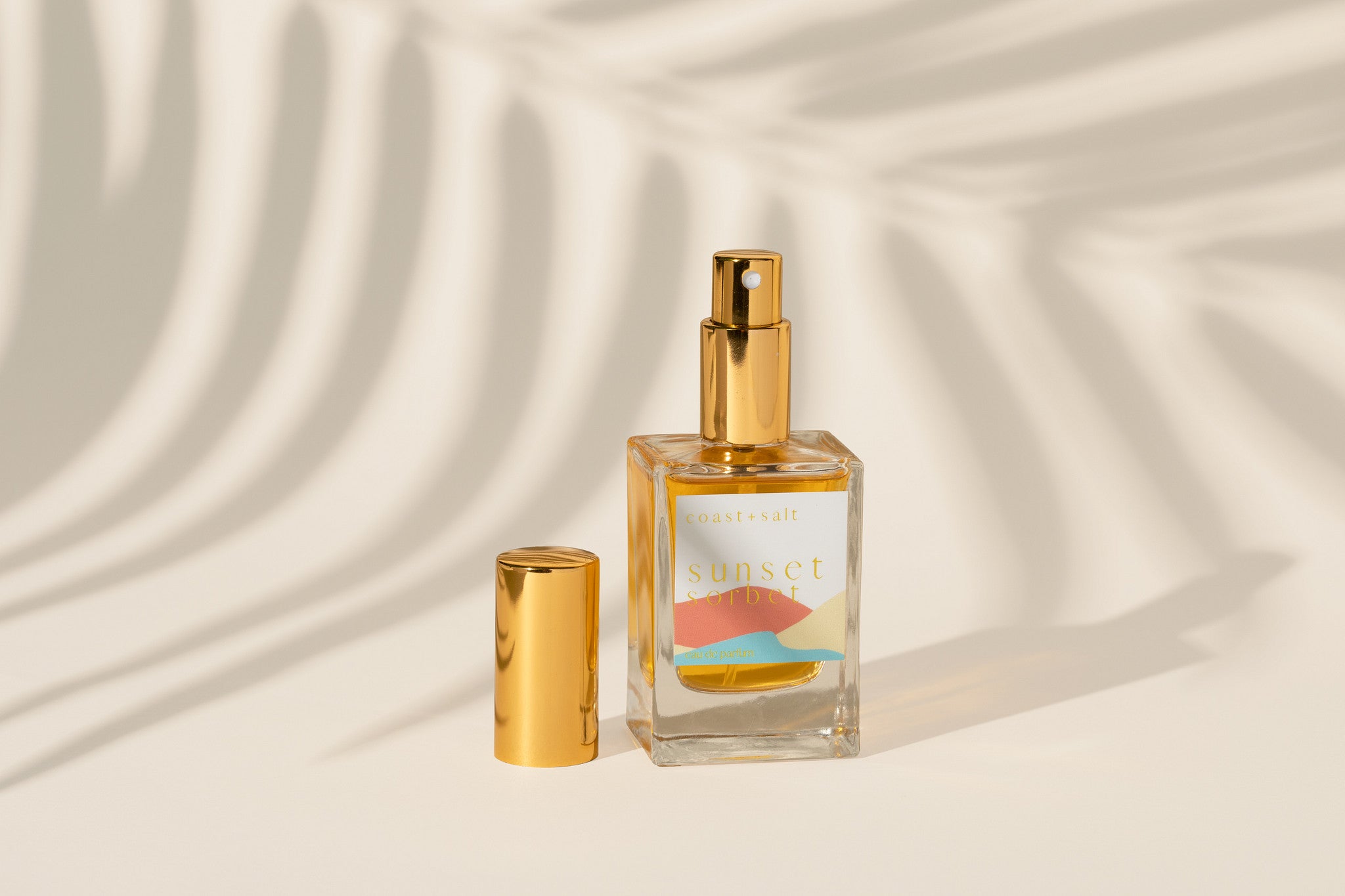 Sunset Sorbet perfume bottle on a beige background with a palm leaf shadow in background