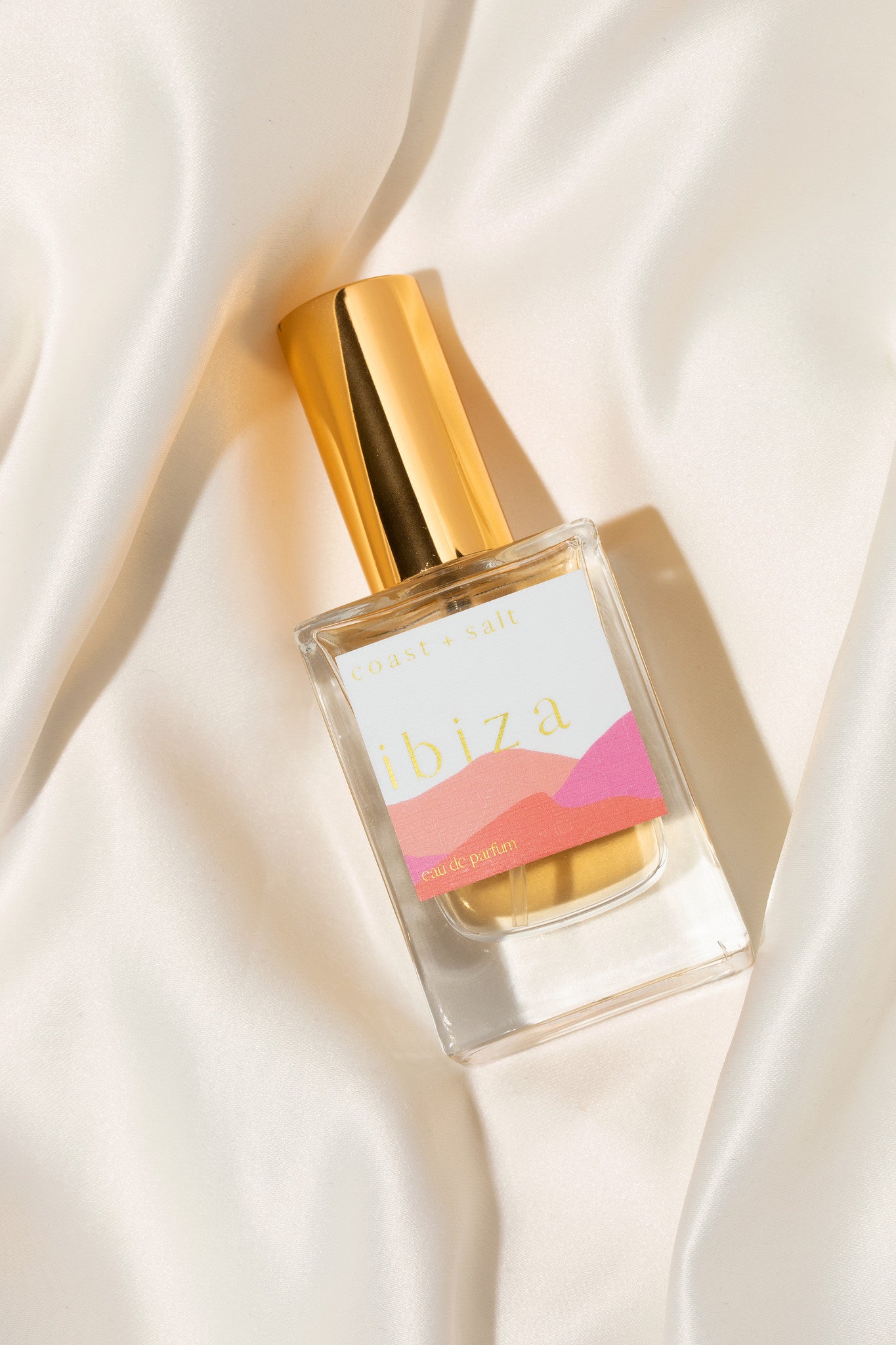 Ibiza Perfume bottle with gold cap and colorful label on a soft white fabric background