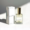 A bottle of Palm Perfume next to the Palm Perfume Retail Box. The box and the perfume bottle are lit in soft daylight, and sitting on a white surface with a diagonal  shadow in the background.