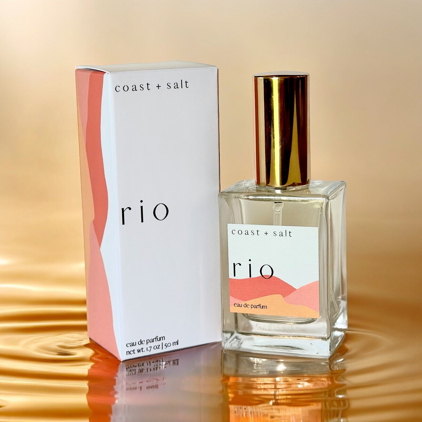 A bottle of Rio Perfume next to the Rio Perfume Retail Box. The box and the perfume bottle are sitting on top of rippling water in an orange hue.